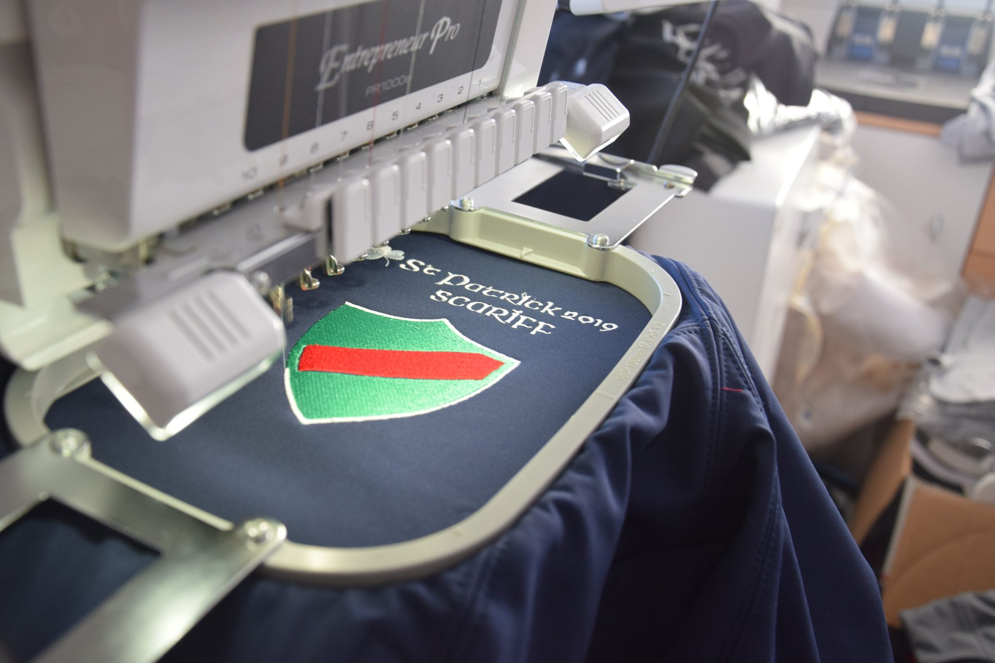 Machine à broder brodant un écusson vert et rouge sur une veste bleue