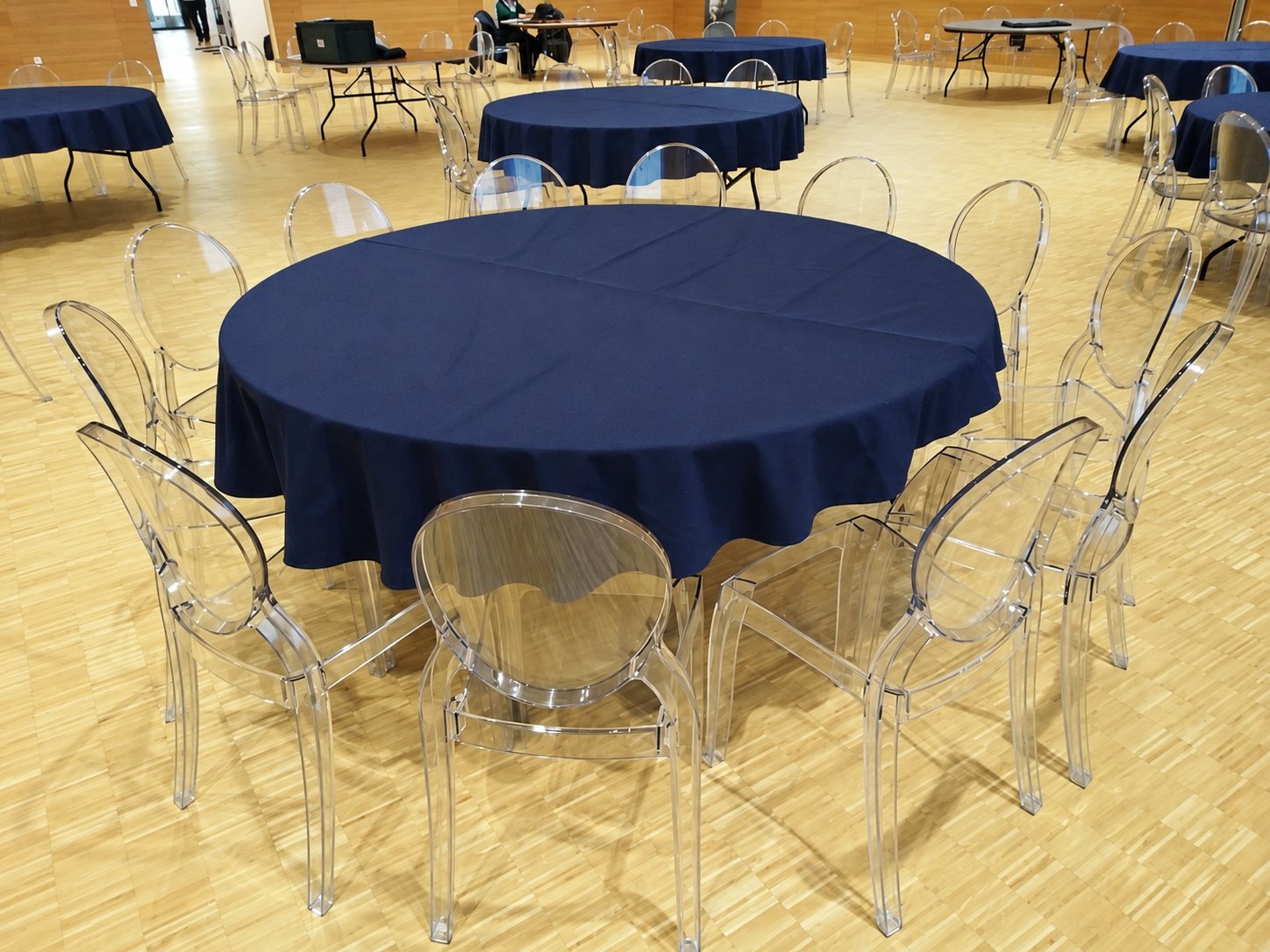 Table ronde nappée de bleu marine entourée de chaises transparentes dans une salle