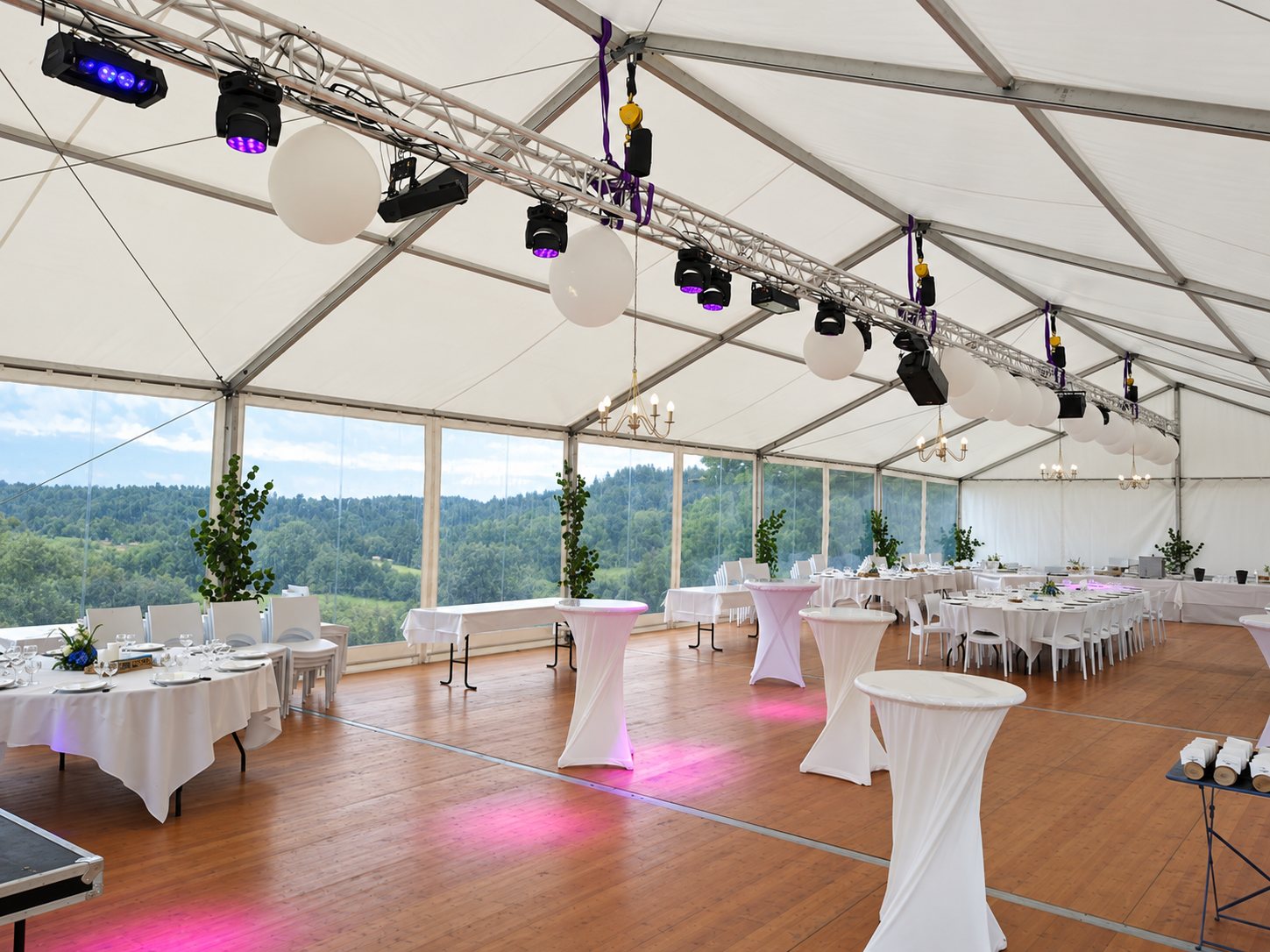 Grande tente de réception aménagée avec tables, éclairages et vue sur la campagne